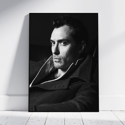 A black and white portrait print of a man in a dark coat leaning against a white wall on a light wood floor.